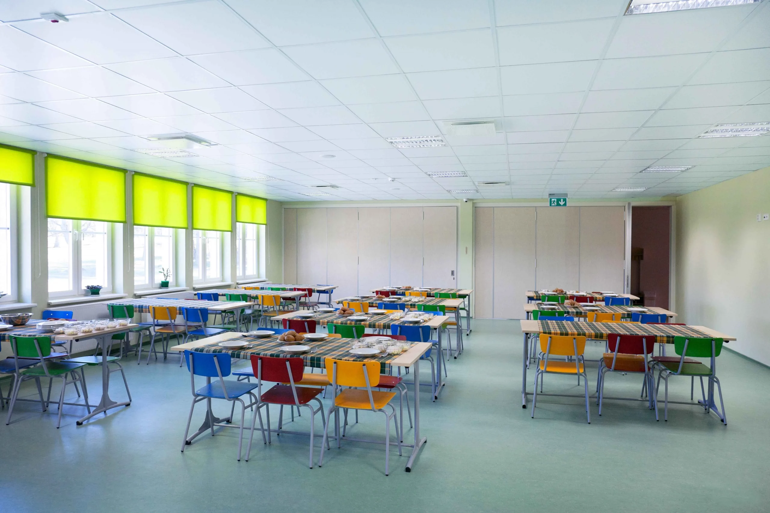 Freundliche Schulmensa mit bunten Stühlen und gedeckten Tischen – frisches Schulessen und Kitaessen von Cook&Clean